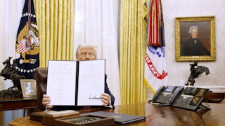 Donald Trump holds up a signed executive order in the Oval Office.