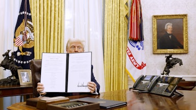 Donald Trump holds up a signed executive order in the Oval Office.