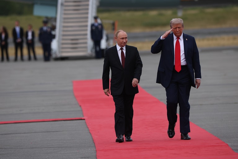 President Donald Trump salutes as he and Russian President Vladimir Putin walk down a red carpet on a military base tarmac in Alaska.