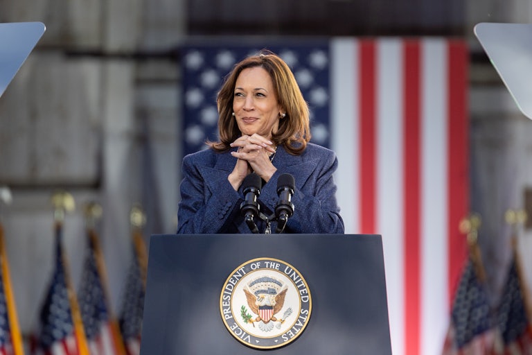 Kamala Harris folds her hands under her chin while standing at a podium