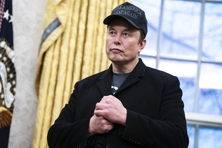 Elon Musk puts his hands together in front of his chest as he stands in the Oval Office in the White House.