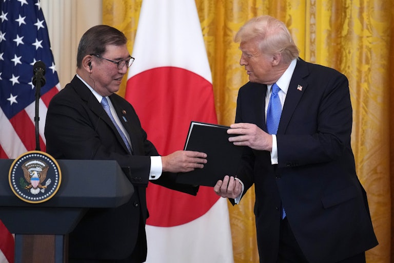 Donald Trump hands a signed photo in a black cover to Japanese Prime Minister Shigeru Ishiba at the White House.