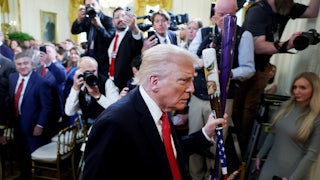 Donald Trump walks with two baseball bats in the White House as reporters take photos of him.
