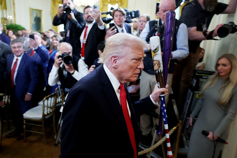 Donald Trump walks with two baseball bats in the White House as reporters take photos of him.