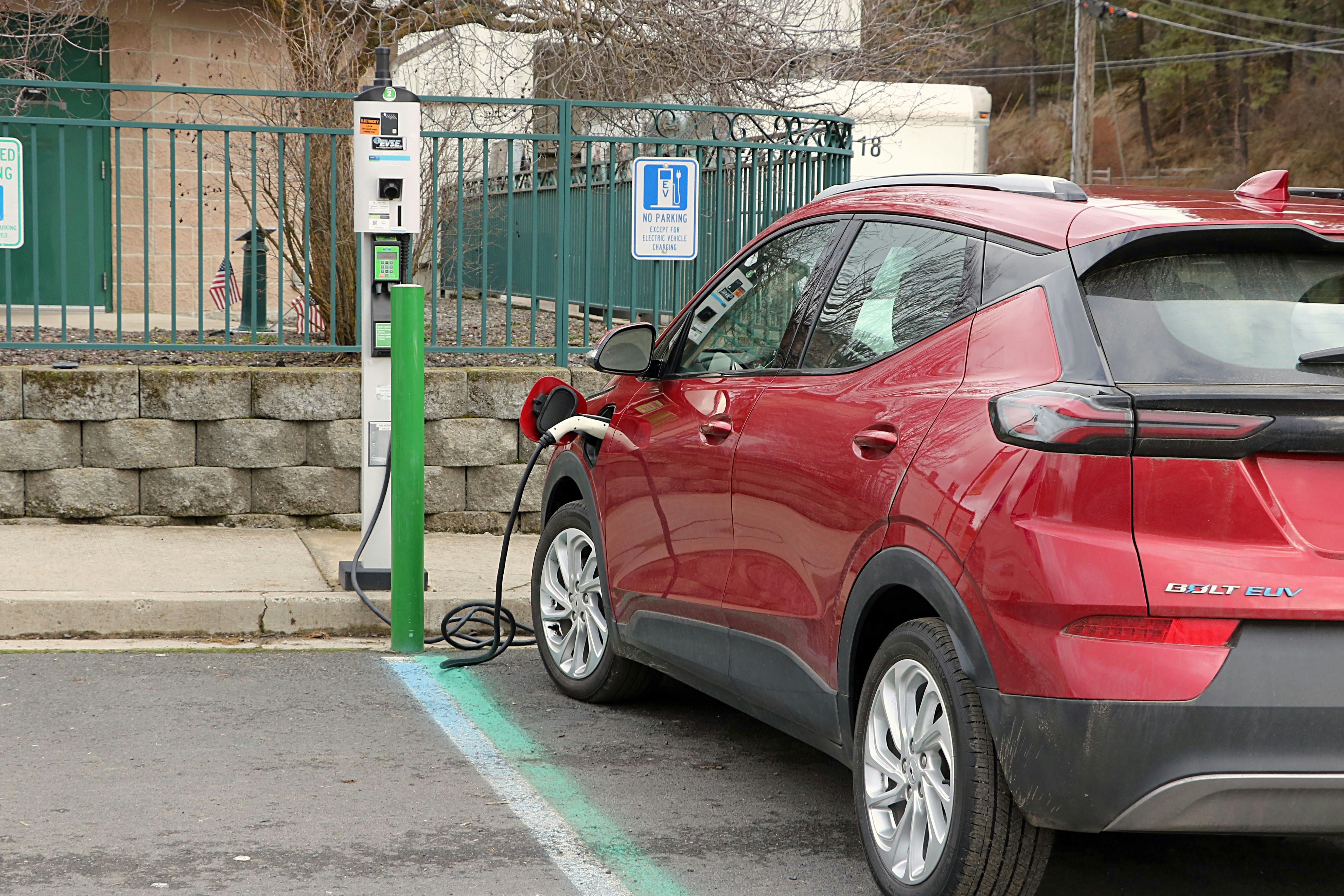 A red Chevrolet Volt is seen in a parking spot with a charging cord coming out of it to a charging station on the curb.