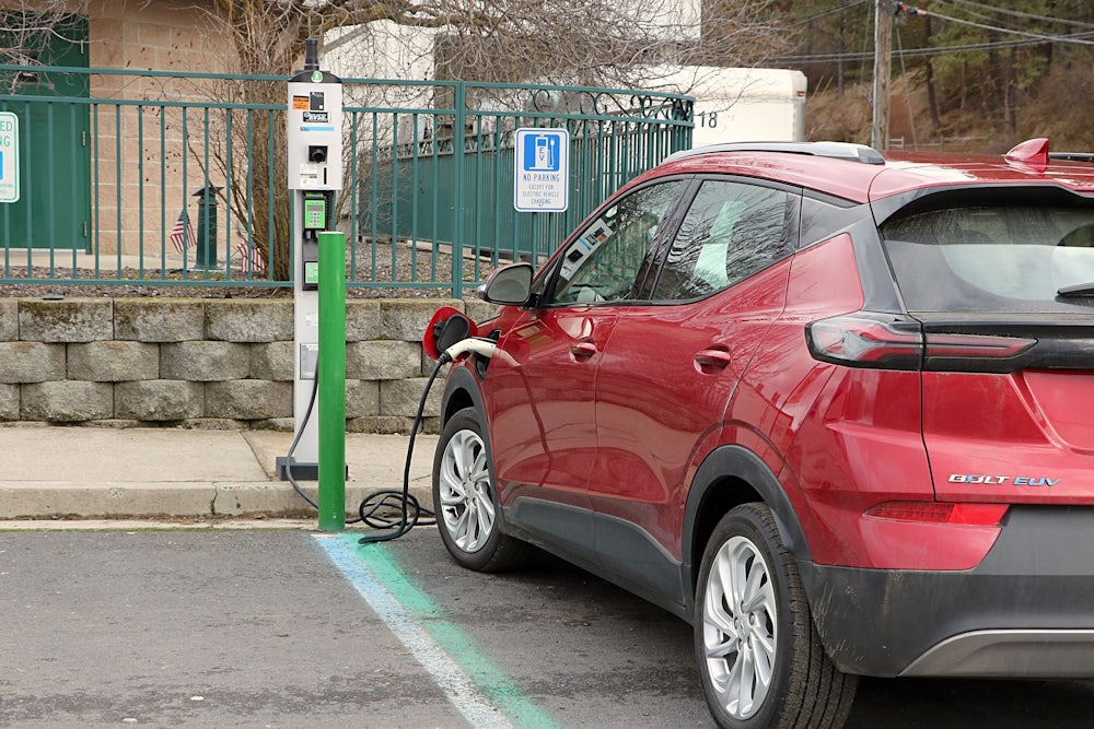 A red Chevrolet Volt is seen in a parking spot with a charging cord coming out of it to a charging station on the curb.