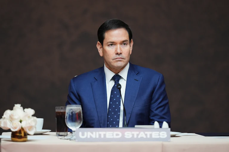Marco Rubio looks uncomfortable as he sits at a table behind a United States nameplate.