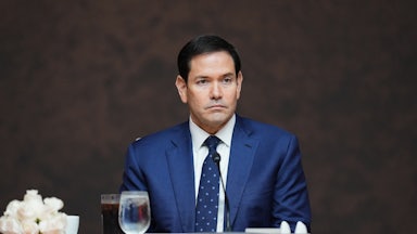 Marco Rubio looks uncomfortable as he sits at a table behind a United States nameplate.
