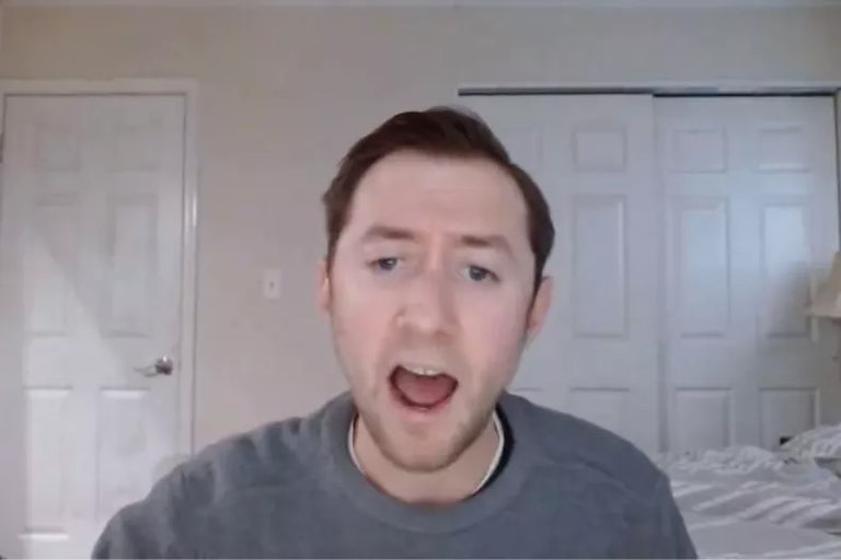 Justin Mohns (a white, young man with brown hair) is in a bedroom yelling at the camera. He wears a gray sweater. Behind him is a white comforter, and three sets of doors.