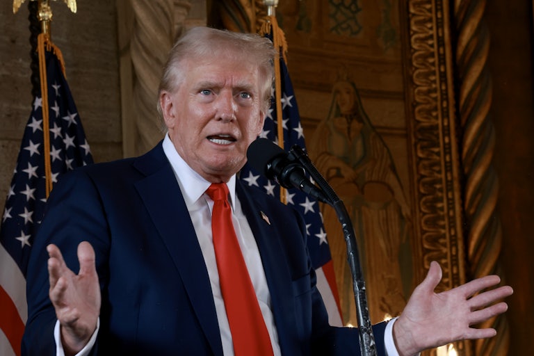 Donald Trump speaks at a mic, his hands splayed out