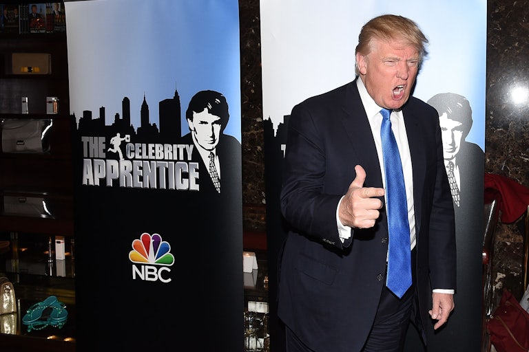 Donald Trump yells and points next to an sign that reads "The Celebrity Apprentice" with a photo of his face and the NBC logo..