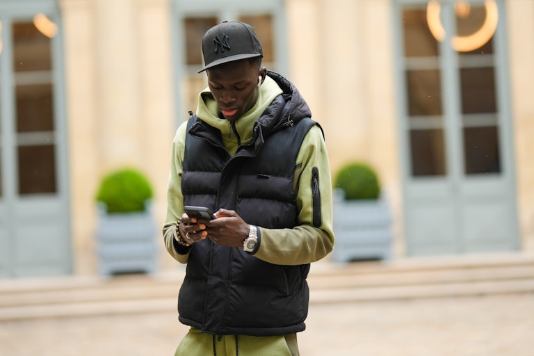 A Black person walking outside looks down at their phone