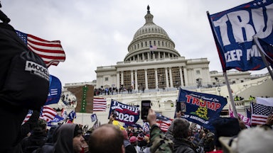 Protesters waving Trump 2020 flags, mob in front of the Capitol building.