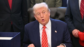 Donald Trump puckers his lips while speaking at his desk in the Oval Office