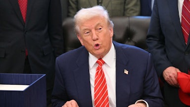 Donald Trump puckers his lips while speaking at his desk in the Oval Office