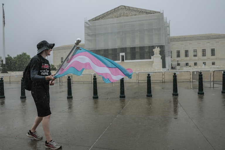 Someone walks in front of the Supreme Court carrying a trans flag.