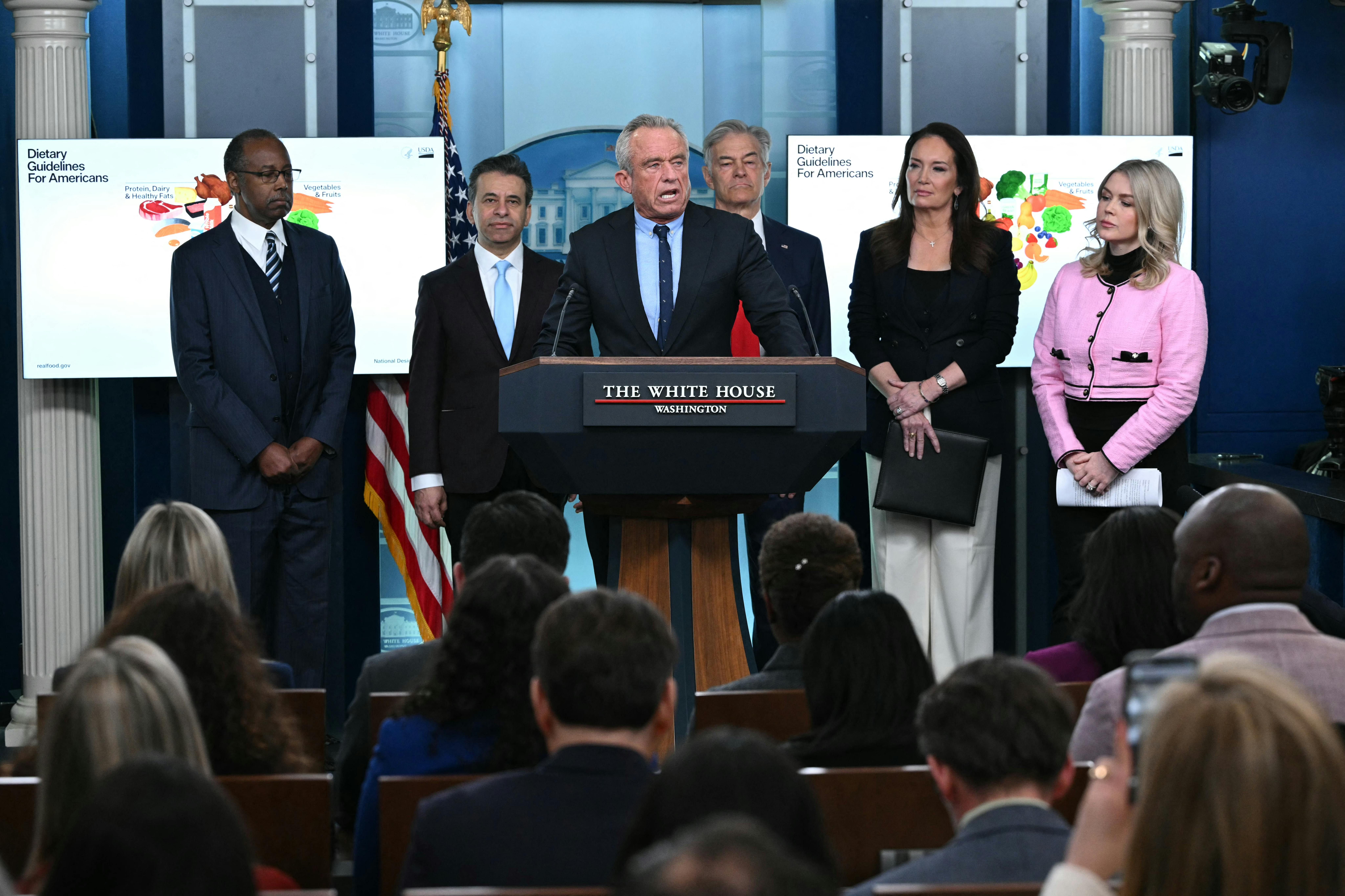 Health Secretary Robert F. Kennedy Jr speaks at the podium in the White House press briefing room. He is flanked by Ben Carson, Marty Makary, Mehmet Oz, Brooke Rollins, and Karoline Leavitt