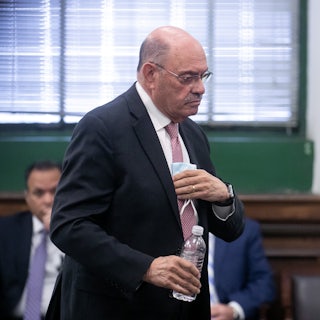 Allen Weisselberg tucks a folded item into his suit pocket and holds a water bottle in his hand