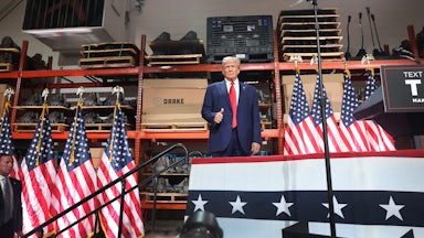 Trump stands on a platform bedecked with American flags in front of automotive parts.