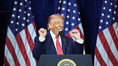 Donald Trump raises his fists and sticks out his tongue while standing at a podium