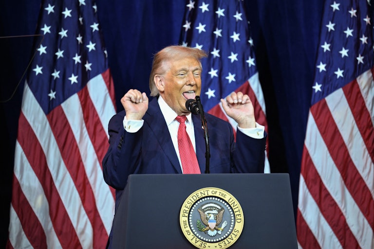 Donald Trump raises his fists and sticks out his tongue while standing at a podium