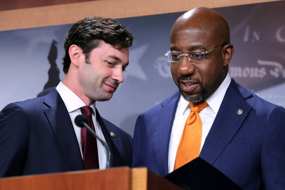 Georgia Senators Jon Ossoff and Raphael Warnock converse behind a lectern.