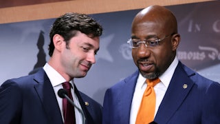 Georgia Senators Jon Ossoff and Raphael Warnock converse behind a lectern.