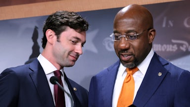 Georgia Senators Jon Ossoff and Raphael Warnock converse behind a lectern.