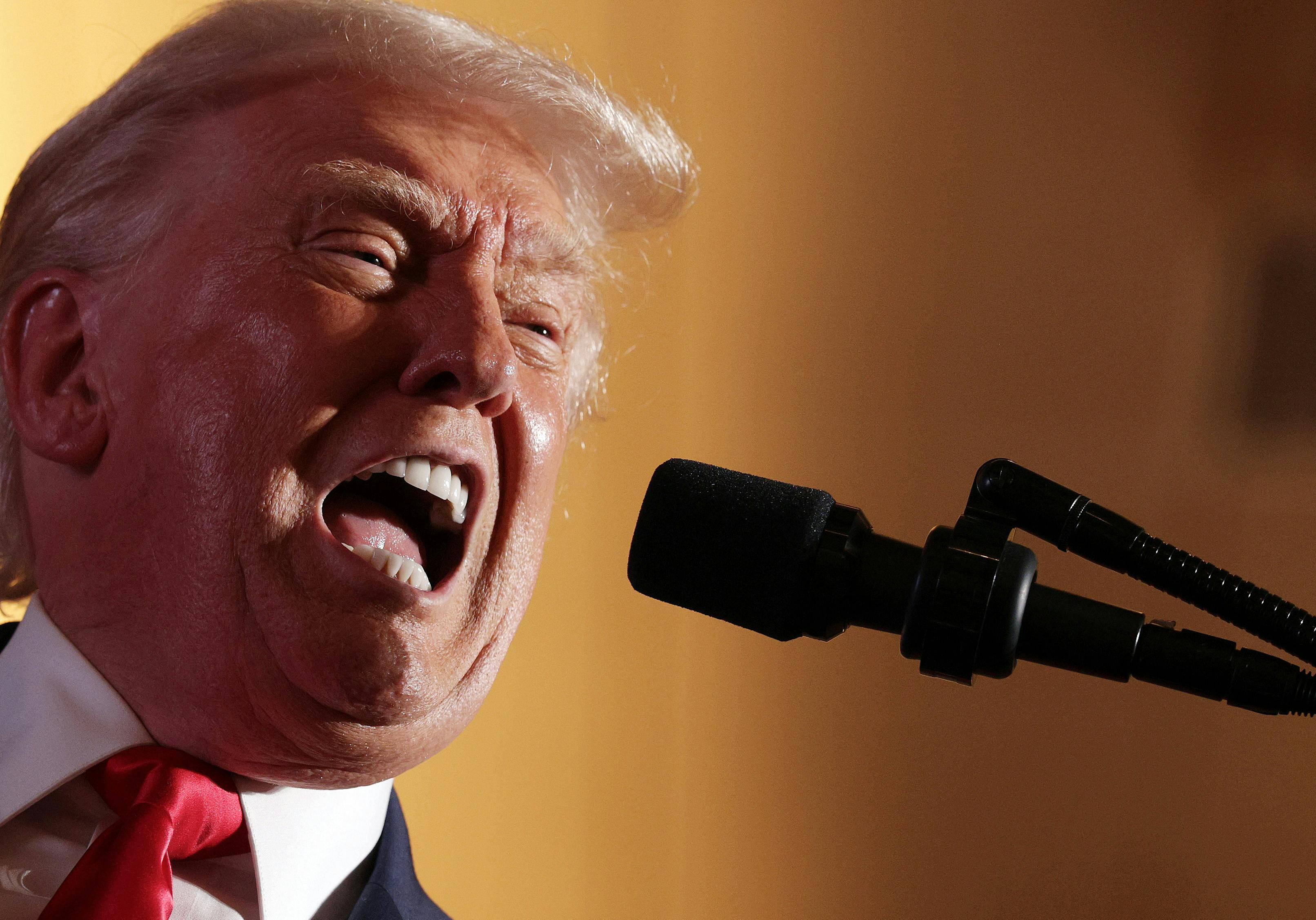 Donald Trump yells into a microphone with wide open mouth