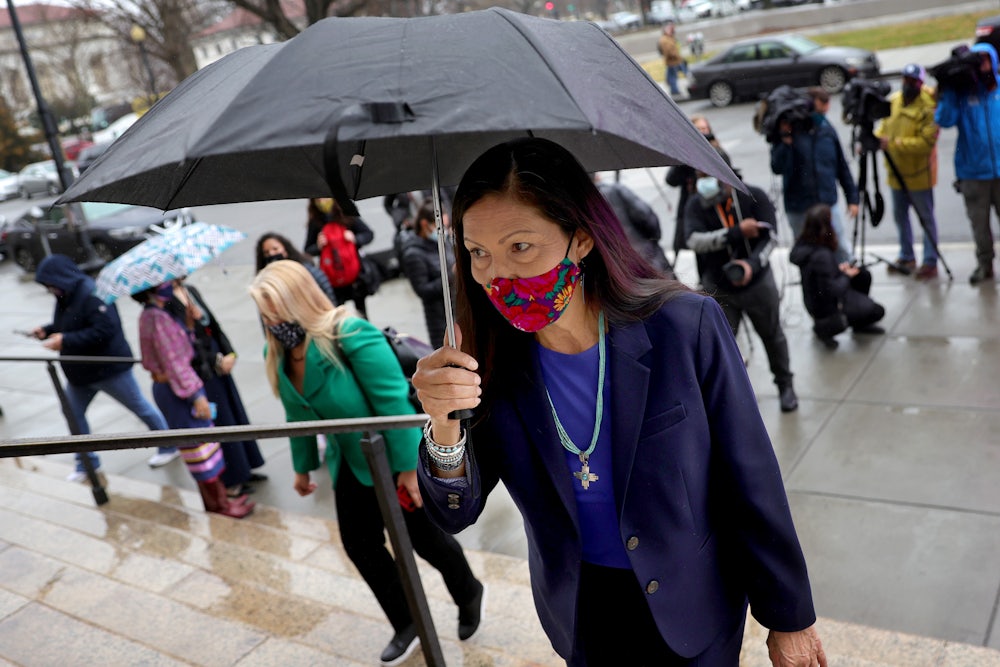 Deb Haaland walks up steps holding an umbrella.