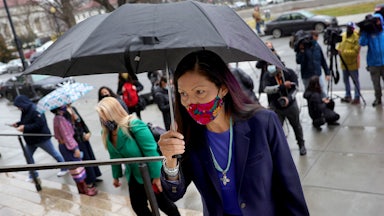 Deb Haaland walks up steps holding an umbrella.