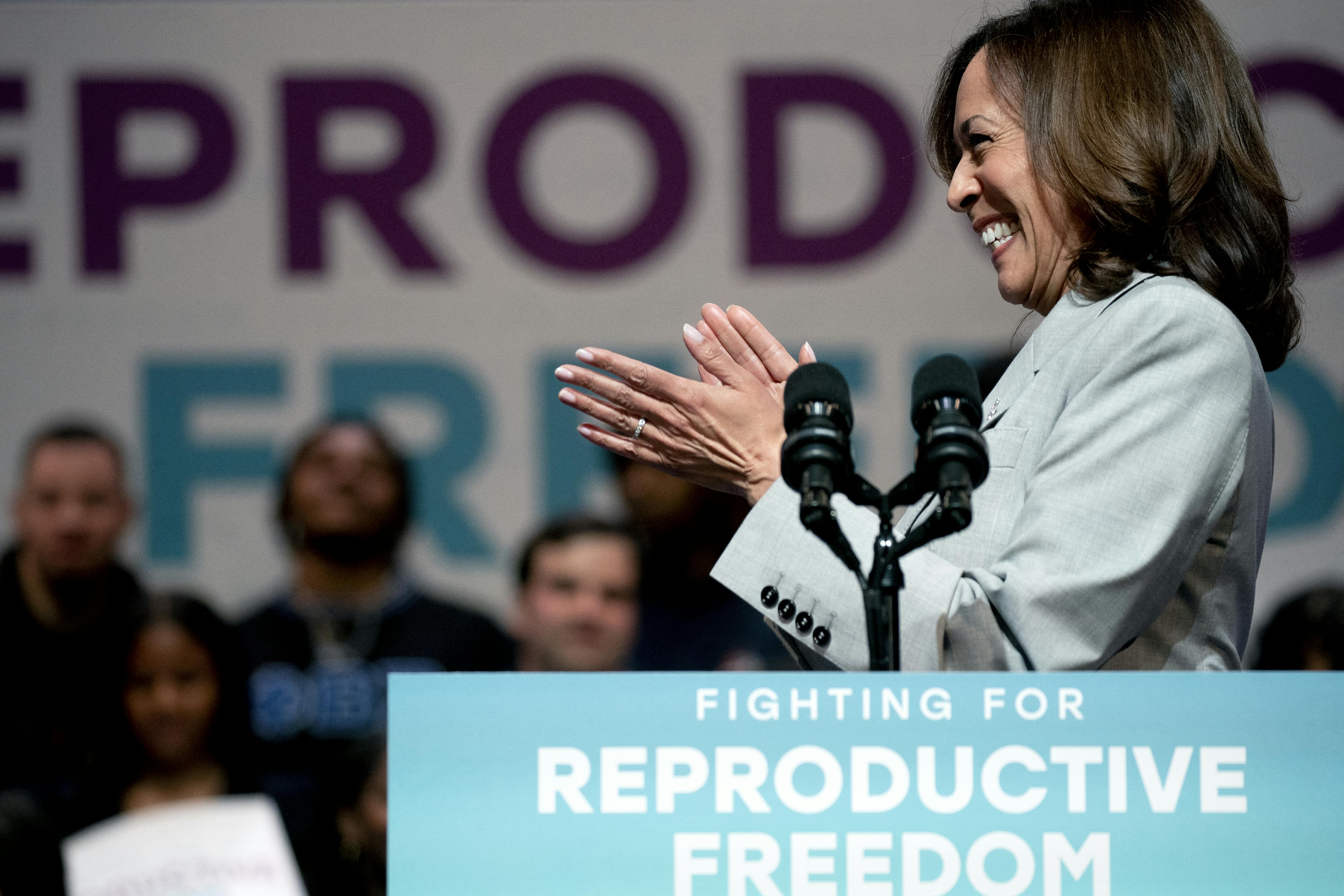 Vice President Kamala Harris smiles and claps in front of a sign touting reproductive freedom.