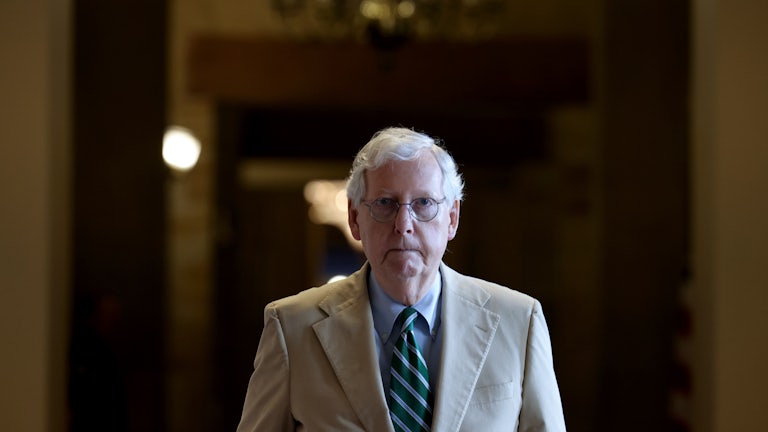 A close-up of Mitch McConnell as he walks down a darkened hallway.