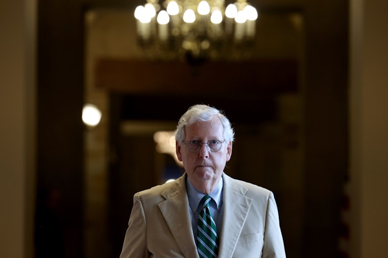 A close-up of Mitch McConnell as he walks down a darkened hallway.