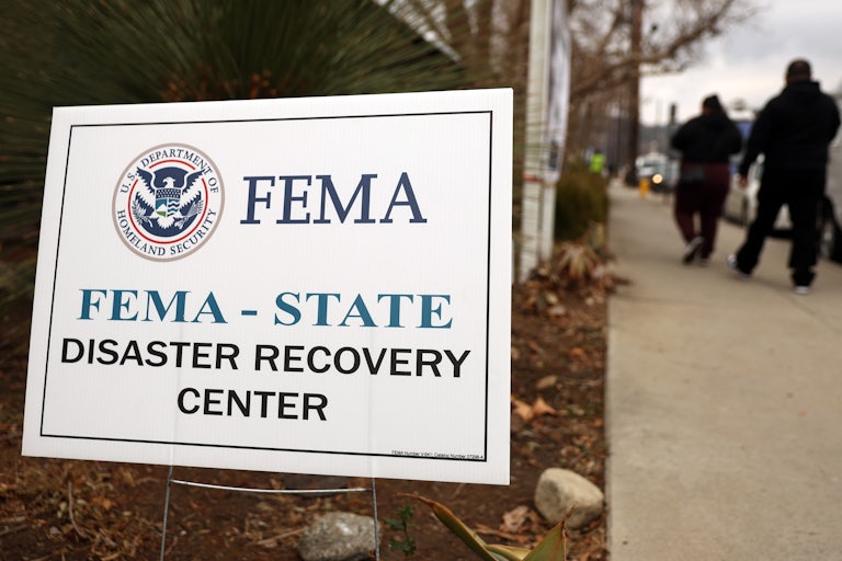 People walk past a sign that reads "FEMA - STATE Disaster Recovery Center)