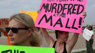 A gun violence protester holds a sign reading "I don't want to be murdered at the mall." Others around her hold signs as well.