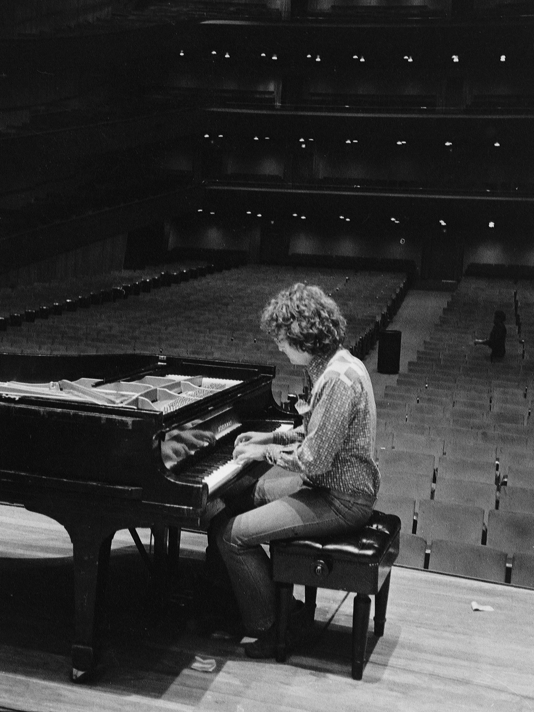 A photo of musician and songwriter Randy Newman at a piano on stage in an empty auditorium