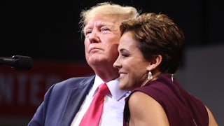 Trump and Kari lake hug while facing an audience.