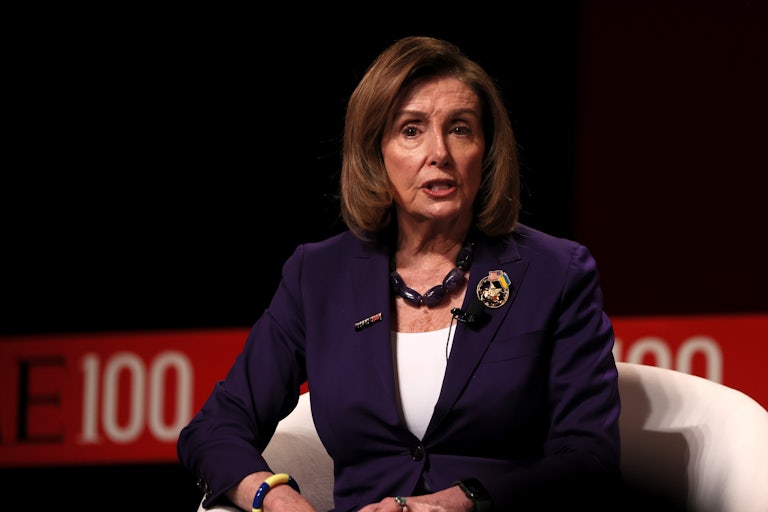 Representative Nancy Pelosi wears a purple blazer and is speaking while seated.