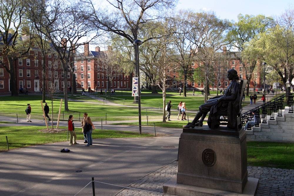 People walk in Harvard Yard next to the John Harvard statue.