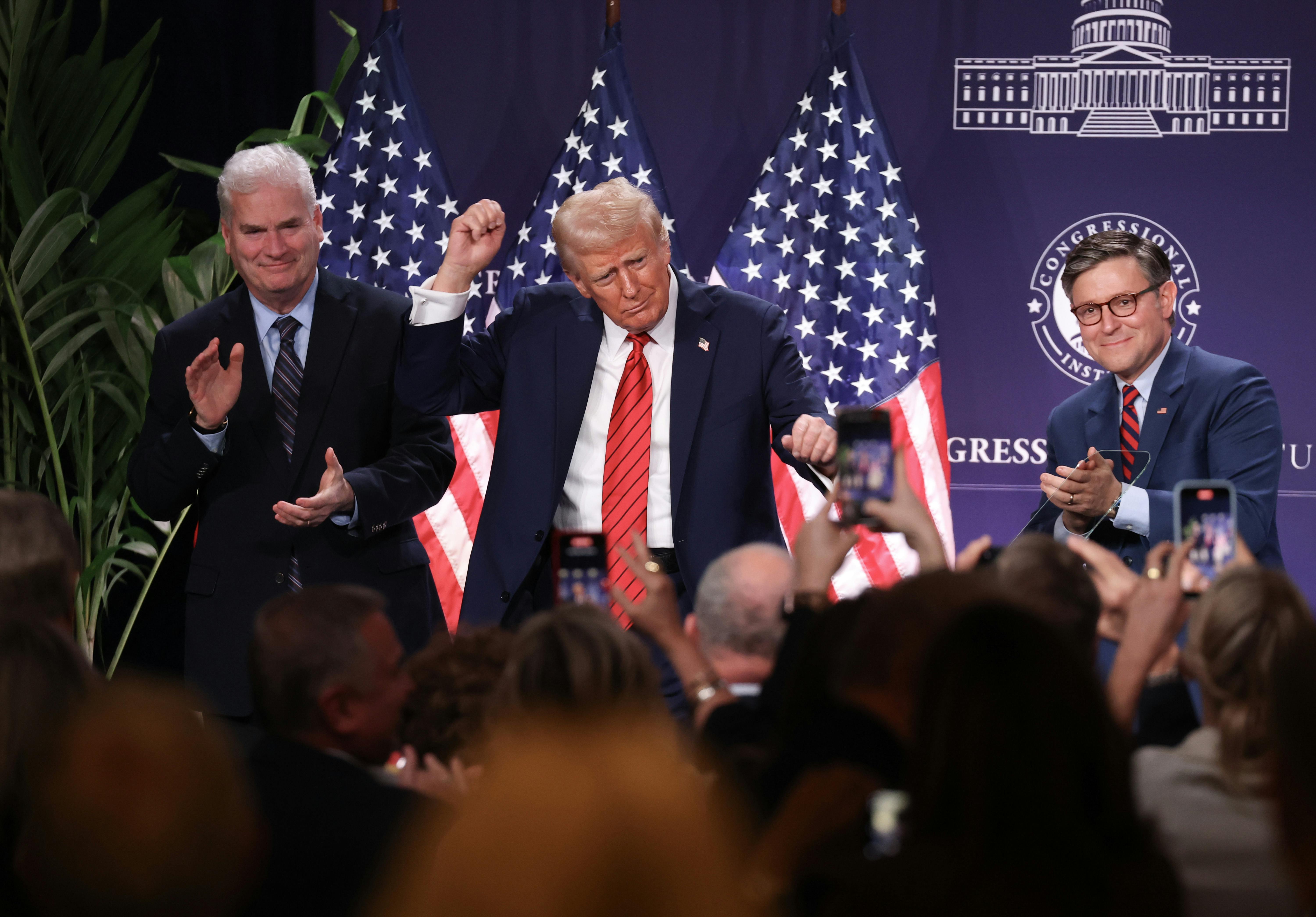 Trump holds his fists up, dancing in front of a crowd, flanked by Tom Emmer and Mike Johnson.