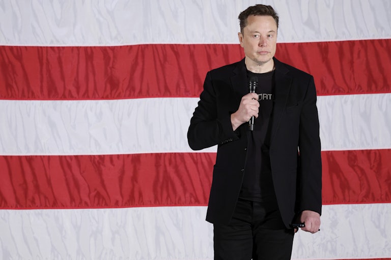Elon Musk stands in front of a giant U.S. flag and makes a weird face