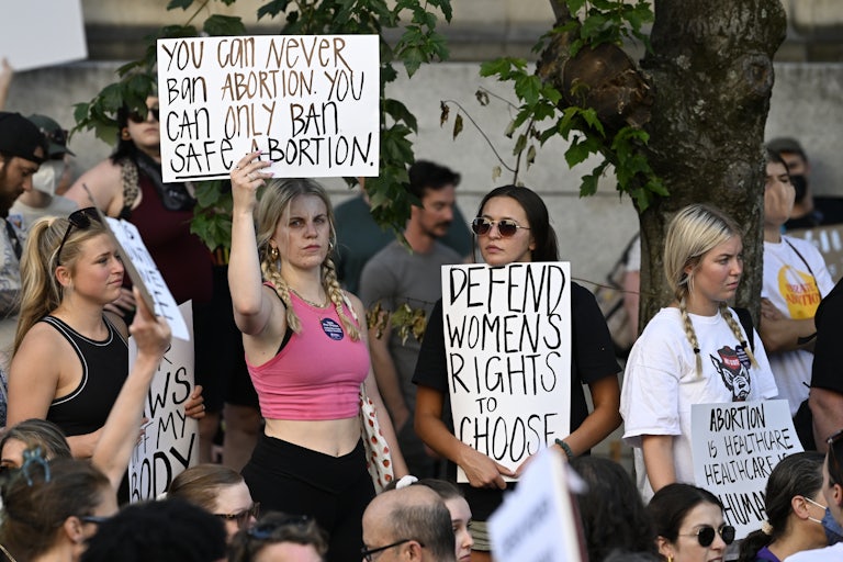 Women protest about abortion. One sign reads "You can never ban abortion. You can only ban safe abortion." Another reads,"Defend womens right to choose."