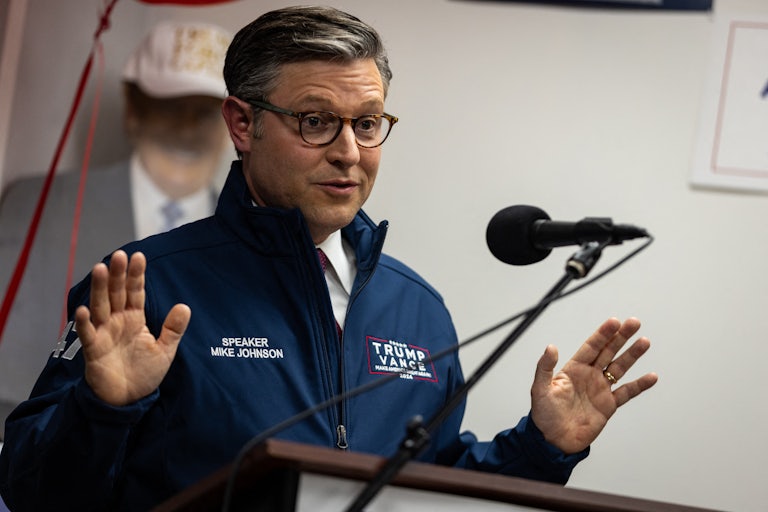 Mike Johnson holds his hands up while speaking into a microphone