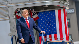 Donald Trump stands on a ledge with lots of American flags