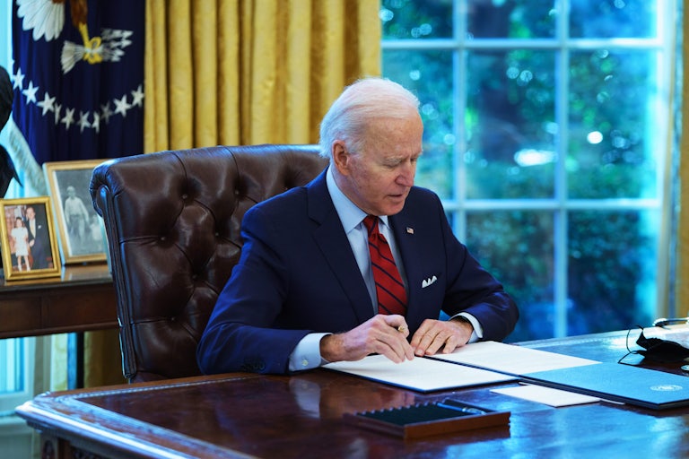 A seated Joe Biden holds a pen in his right hand while preparing to sign an executive order in the Oval Office 