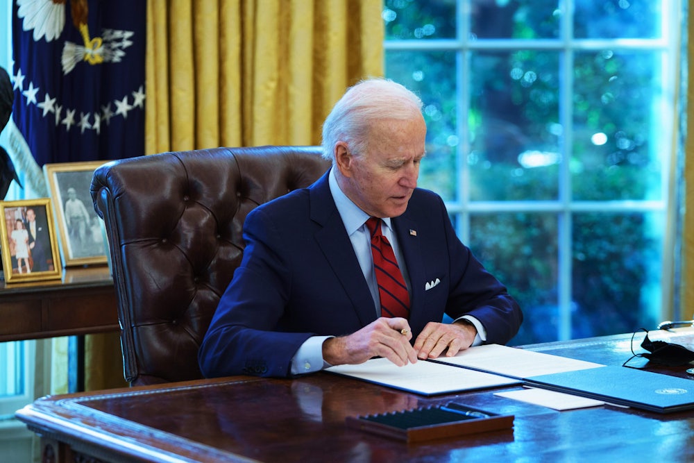 A seated Joe Biden holds a pen in his right hand while preparing to sign an executive order in the Oval Office