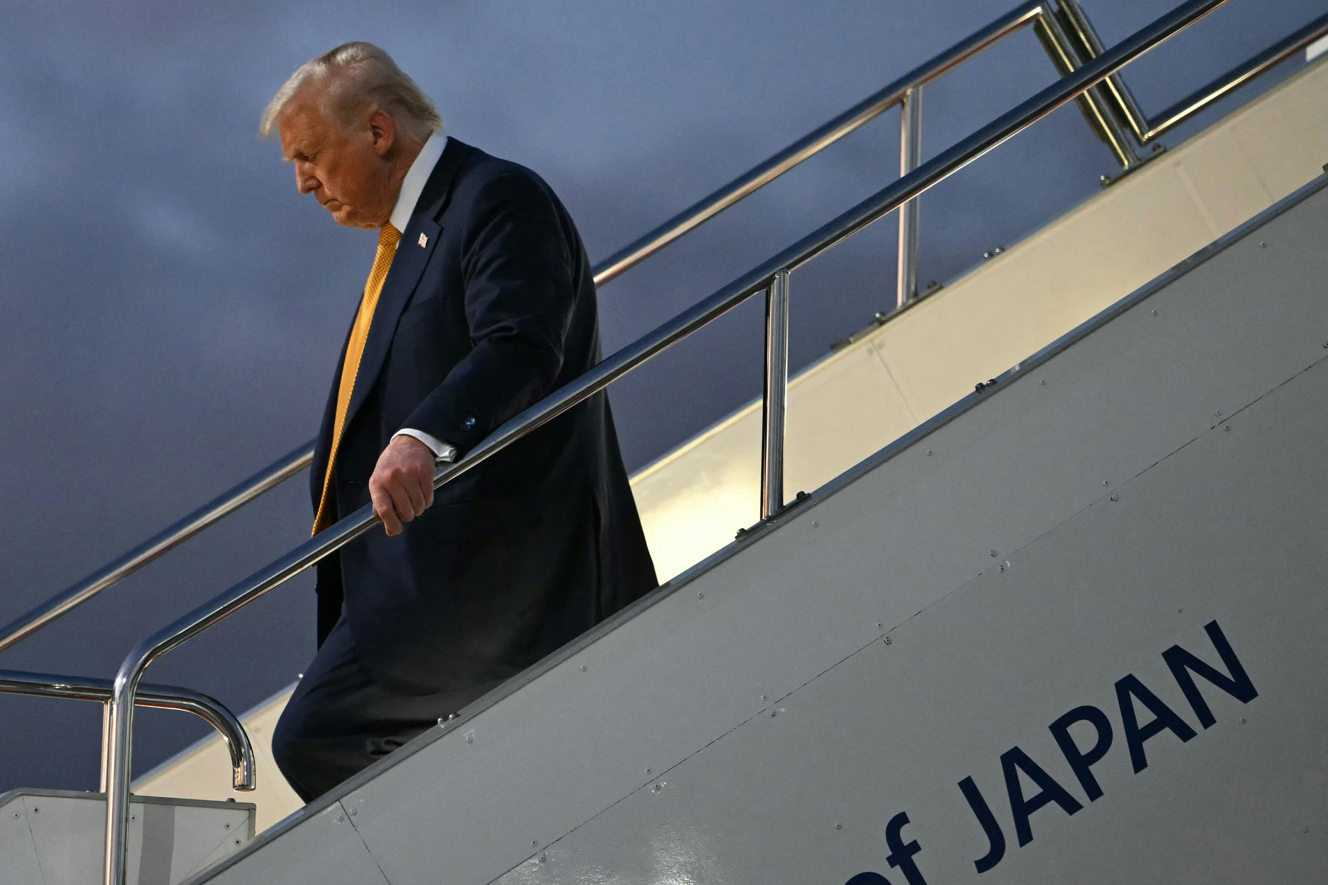 Donald Trump looks down while walking down a flight of stairs off an airplane