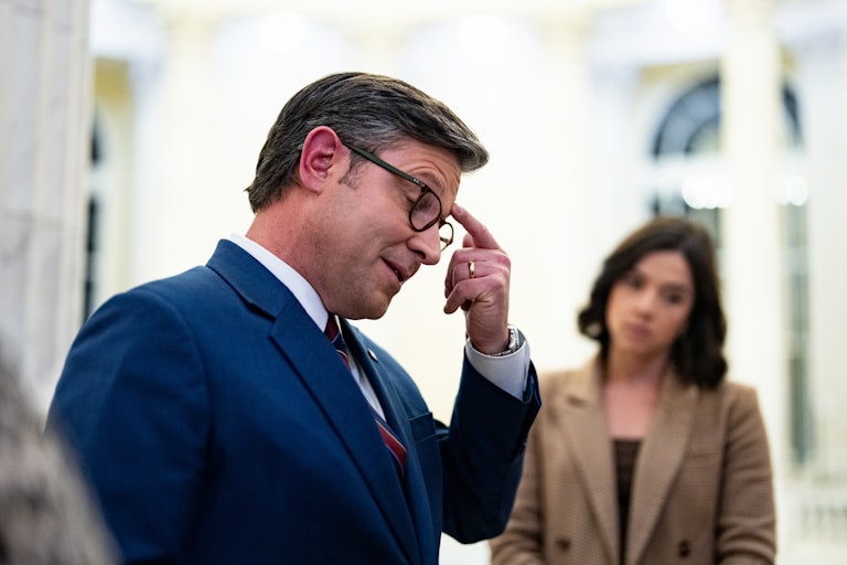 House Speaker Mike Johnson touches his forehead and looks down while speaking to reporters in the Capitol