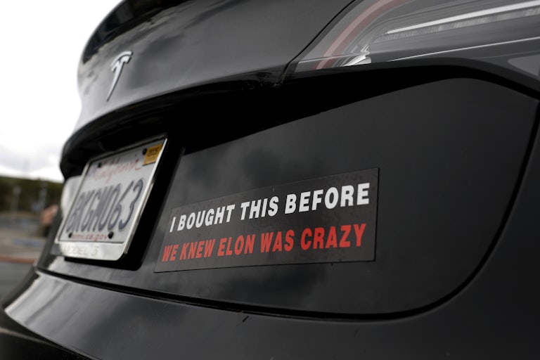 A bumper sticker on a Tesla says, "I bought this before we knew Elon was crazy"